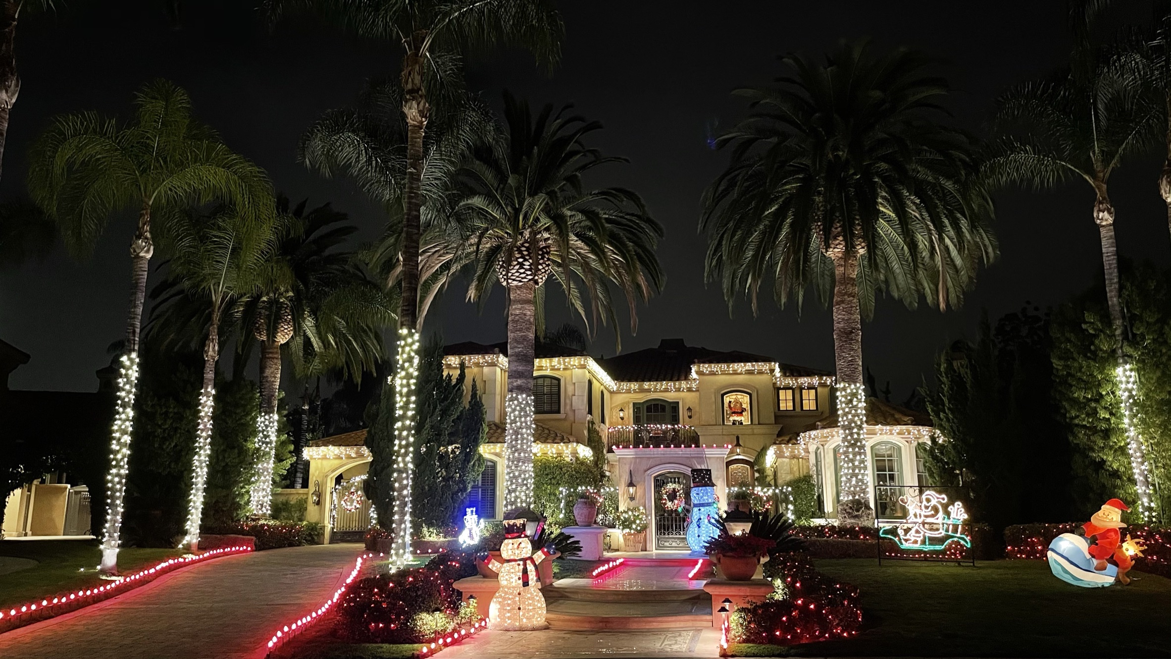 Palm-lined property with Christmas roofline lights, wrapped palms, and illuminated holiday decorations